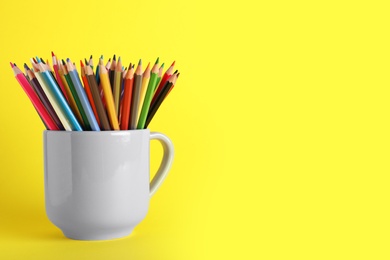 Colorful pencils in light cup on yellow background. Space for text