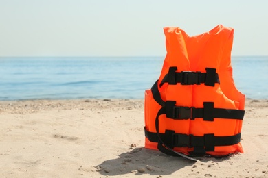 Orange life jacket on sandy beach near sea. Emergency rescue equipment