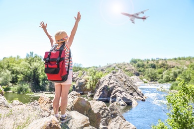 Little girl near river and airplane in sky. Summer vacation