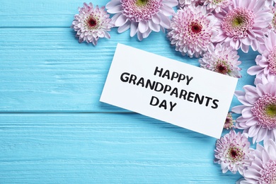 Beautiful flowers and card with phrase Happy Grandparents Day on light blue wooden background, flat lay. Space for text