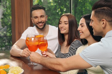 Friends clinking glasses of Aperol spritz cocktails at table
