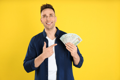 Happy man with cash money on yellow background