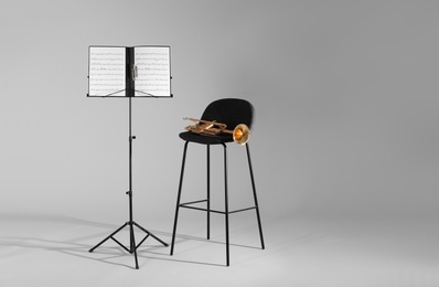 Trumpet, chair and note stand with music sheets on grey background. Space for text