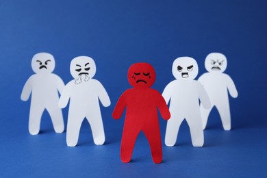 White paper figures and one red on blue background. Bullying concept