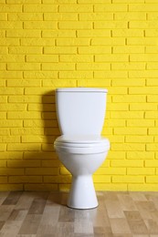 New clean toilet bowl near yellow brick wall indoors. Interior design