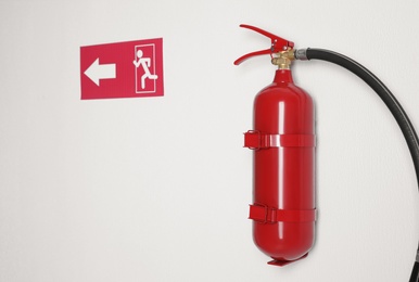 Fire extinguisher and emergency exit sign on white wall