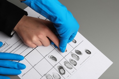 Investigator taking fingerprints of suspect at table, closeup. Criminal expertise