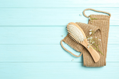 Hair brush, bast wisp and small white flowers on light blue wooden background, flat lay. Space for text