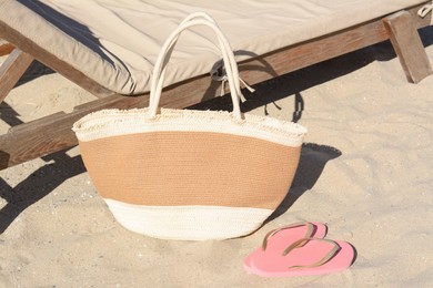 Straw bag and flip flops near wooden sunbed on sandy beach. Summer accessories