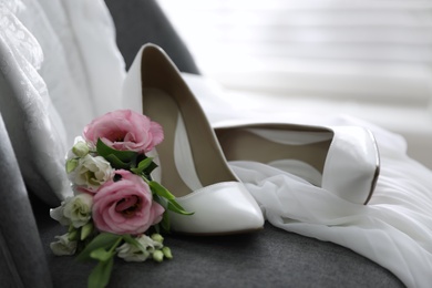 Pair of white high heel shoes, flowers and wedding dress on chair indoors