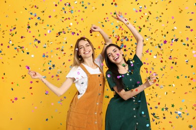 Happy women and falling confetti on yellow background