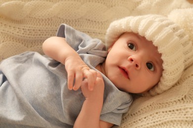 Cute little baby wearing white warm hat on knitted blanket