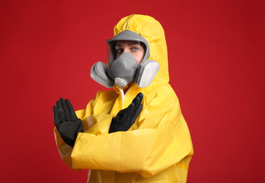 Woman in chemical protective suit making stop gesture on red background. Virus research