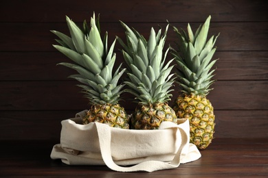 Photo of Bag with fresh juicy pineapples on wooden table