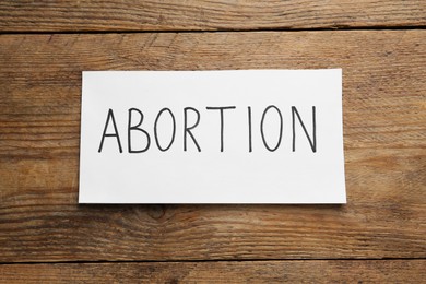 Paper note with word Abortion on wooden background, top view