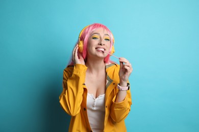 Fashionable young woman in pink wig with headphones chewing bubblegum on yellow background