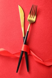 Photo of Cutlery set with ribbon on red background, flat lay. Romantic table setting