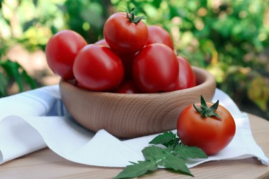 Bowl and fresh tomatoes on wooden table outdoors, closeup
