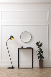 Photo of Console table, houseplant and lamp near light wall with mirror indoors. Interior design