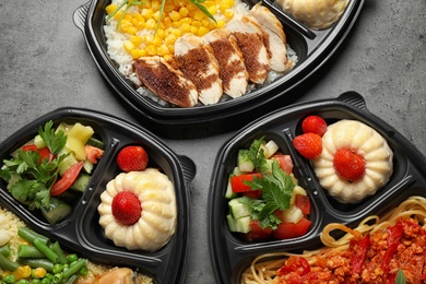 Lunchboxes with different meals on grey table, flat lay. Healthy food delivery