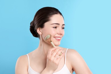 Photo of Young woman massaging her face with jade roller on turquoise background