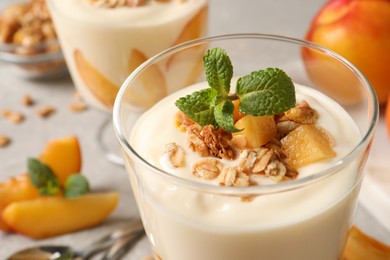 Tasty peach yogurt with granola, mint and pieces of fruit in glass on table, closeup