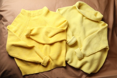Photo of Beautiful yellow warm sweaters on brown bedsheet, flat lay