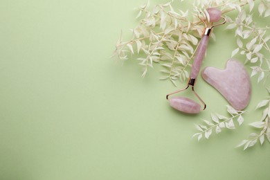 Rose quartz gua sha tool and facial roller on light green background, flat lay. Space for text