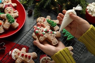 Photo of Making homemade Christmas cookies. Girl decorating gingerbread man at black table, closeup
