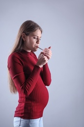 Young pregnant woman smoking cigarette on grey background. Harm to unborn baby