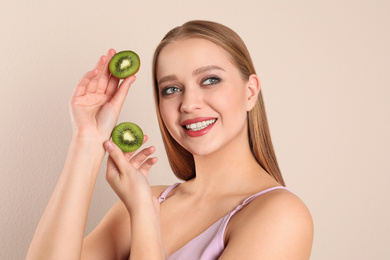Photo of Young woman with cut kiwi on beige background. Vitamin rich food