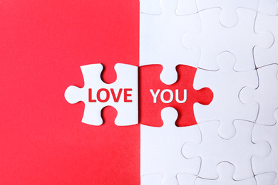 White puzzle with separated piece and phrase LOVE YOU on red background, top view
