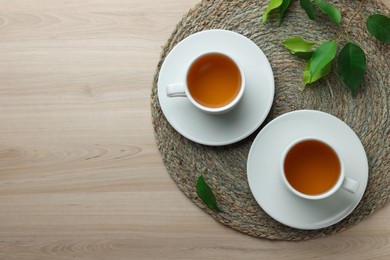 Green tea in white cups with leaves and wicker mat on wooden table, flat lay. Space for text