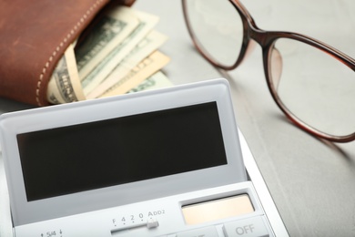 Calculator, glasses and wallet with money on grey table, closeup. Tax accounting