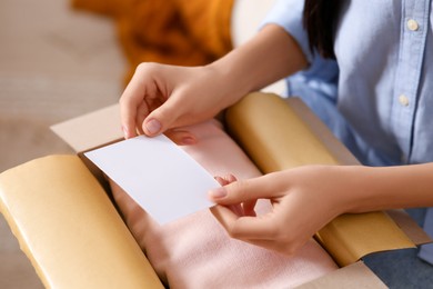 Photo of Woman holding blank greeting card near package with gift, closeup