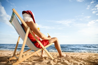 Photo of Santa Claus relaxing in chair on beach, space for text. Christmas vacation