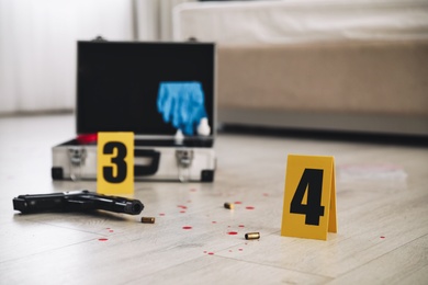 Crime scene markers, gun and criminologist case on floor in room