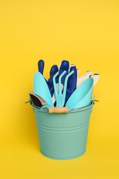 Bucket with gardening gloves and tools on yellow background
