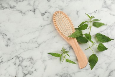 Photo of Stinging nettle and brush on white marble background, flat lay with space for text. Natural hair care