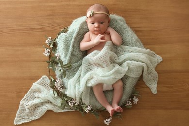 Adorable little baby with green blanket and floral decor on wooden background, top view
