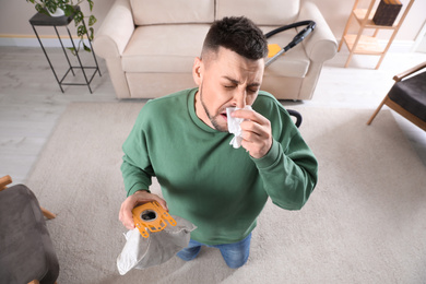 Man with vacuum cleaner bag suffering from dust allergy at home, above view