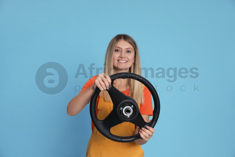 Happy young woman with steering wheel on light blue background