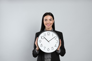 Businesswoman holding clock on light grey background. Time management