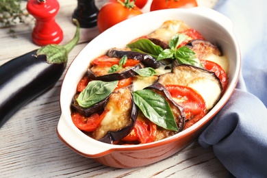Baked eggplant with tomatoes, cheese and basil in dishware on table, closeup