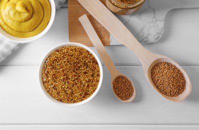 Photo of Bowls and spoons of whole grain mustard with seeds on white wooden table, flat lay