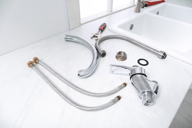 Photo of Parts of water tap and wrench on white marble countertop in kitchen