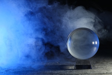 Magic crystal ball  on grey table and smoke against dark background, space for text. Making predictions