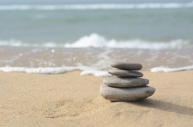 Stack of stones on sandy beach near sea, space for text
