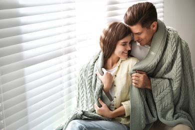 Happy couple covered with warm green plaid near window indoors