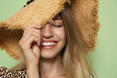 Beautiful young woman wearing straw hat on light green background, closeup. Stylish headdress